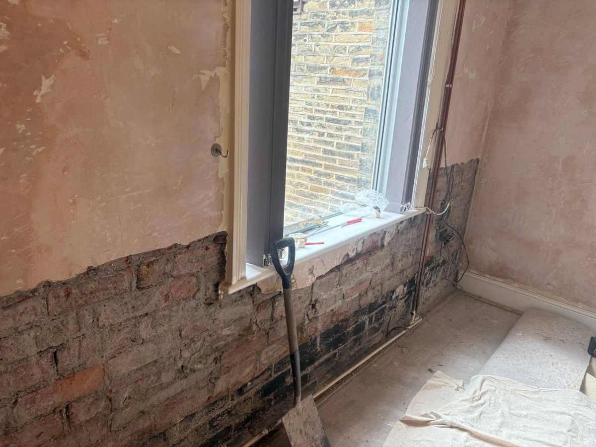 Stained wall stripped back to exposed brick below a window during rising damp treatment