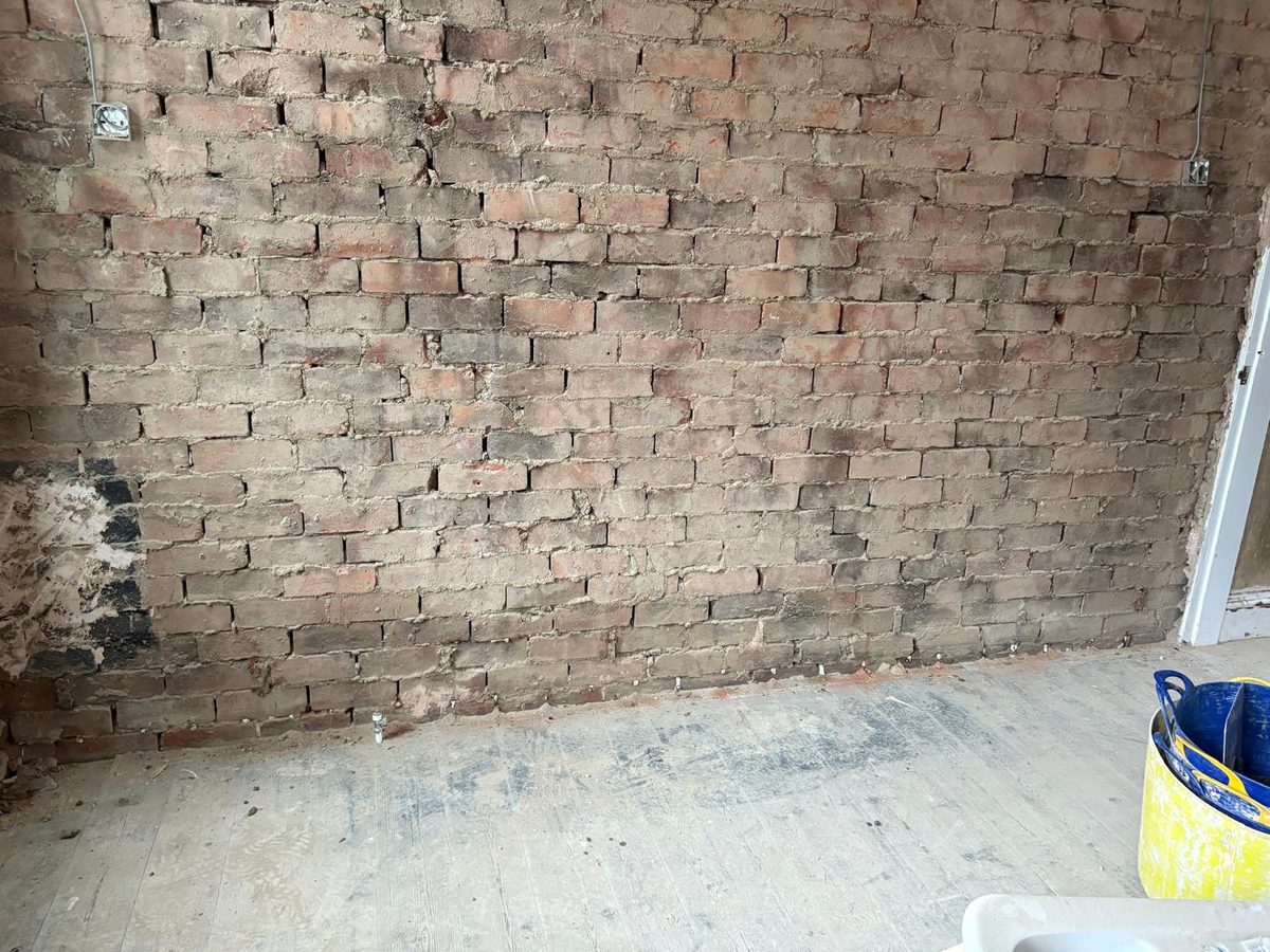 Contaminated plaster stripped back to expose the full brick wall, floorboards protected below