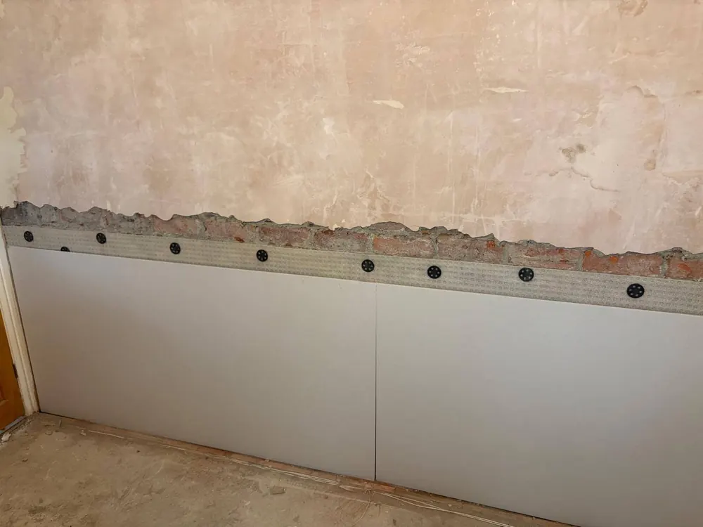 A row of plugged damp proof course injection holes along a wall, with the lower wall covered ready for replastering