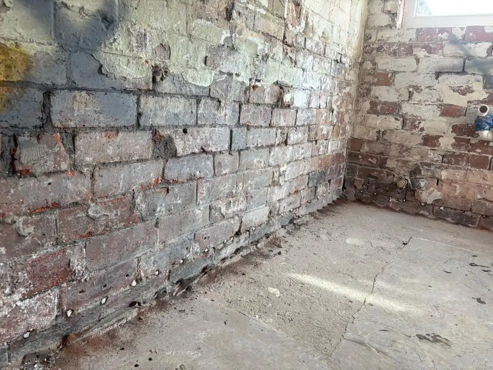 Damp proof course injection holes drilled along the base of a stripped brick wall