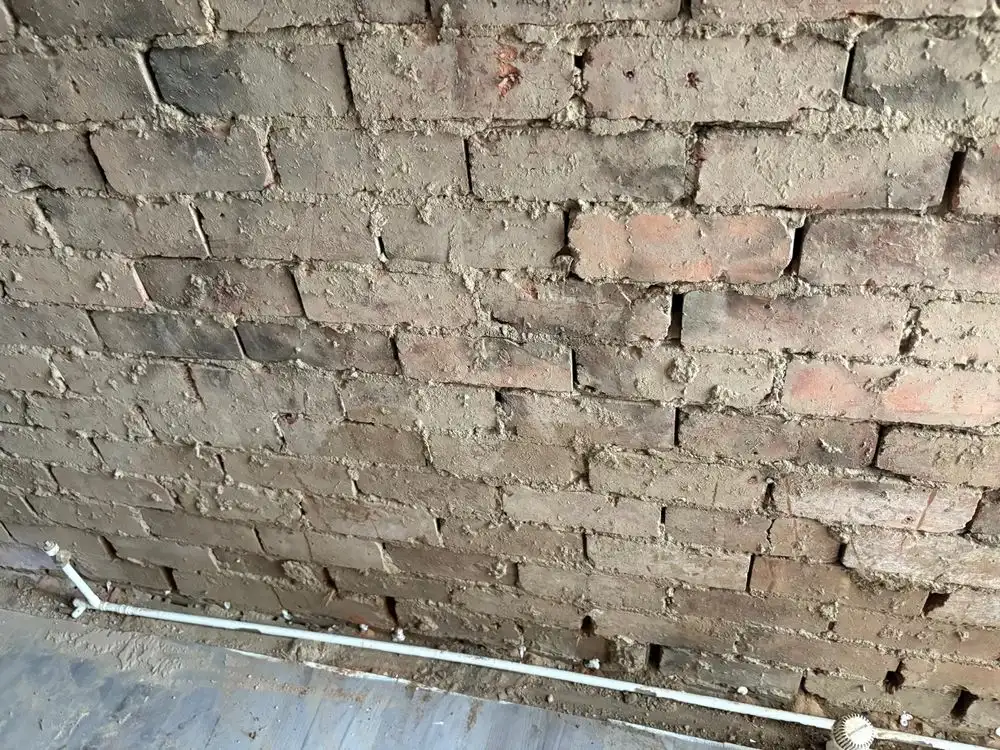 Damp proof course injection holes drilled along the mortar bed of a stripped brick wall