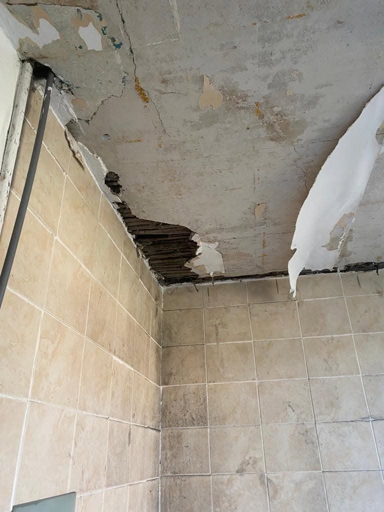A bathroom ceiling that has come away, with laths exposed above tiled walls