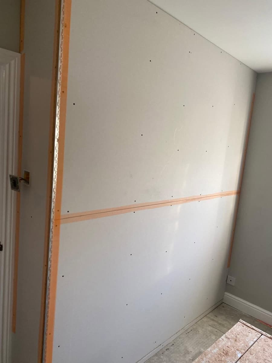 A timber-framed partition wall covered in plasterboard with taped joints, before skimming