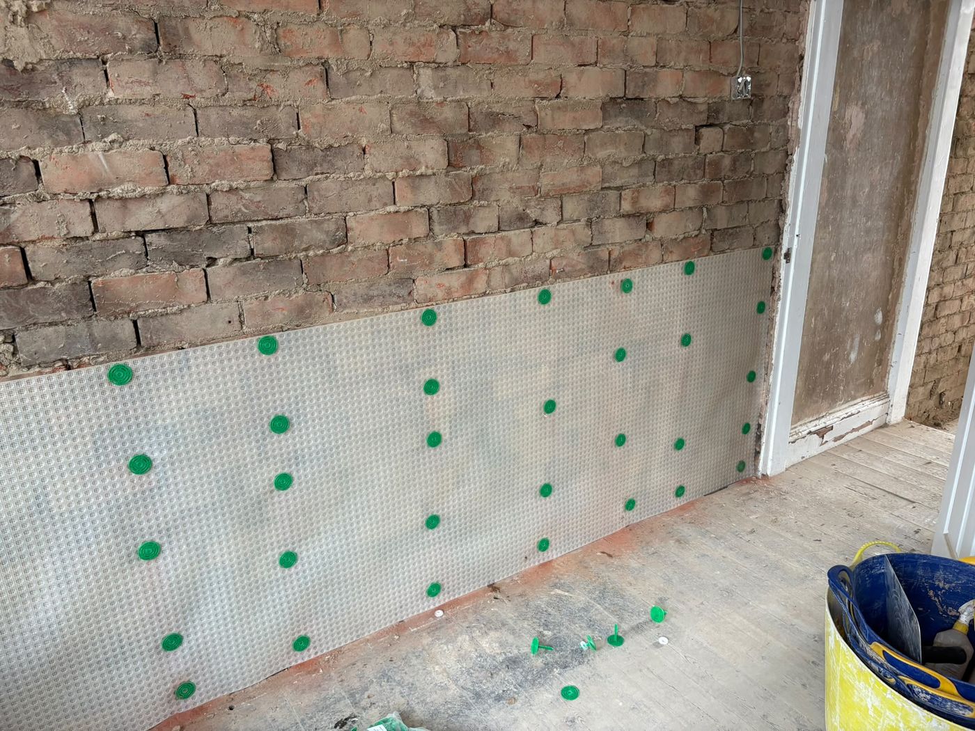 Meshed damp proof membrane fixed to the lower half of a brick wall beside a doorway