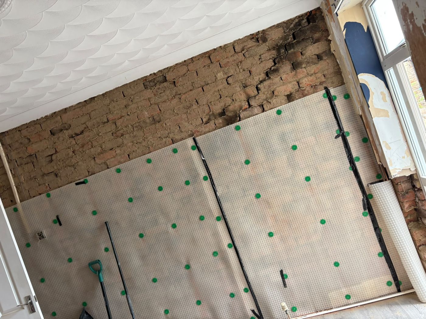 A complete wall covered in meshed damp proof membrane with taped joints, ready for replastering