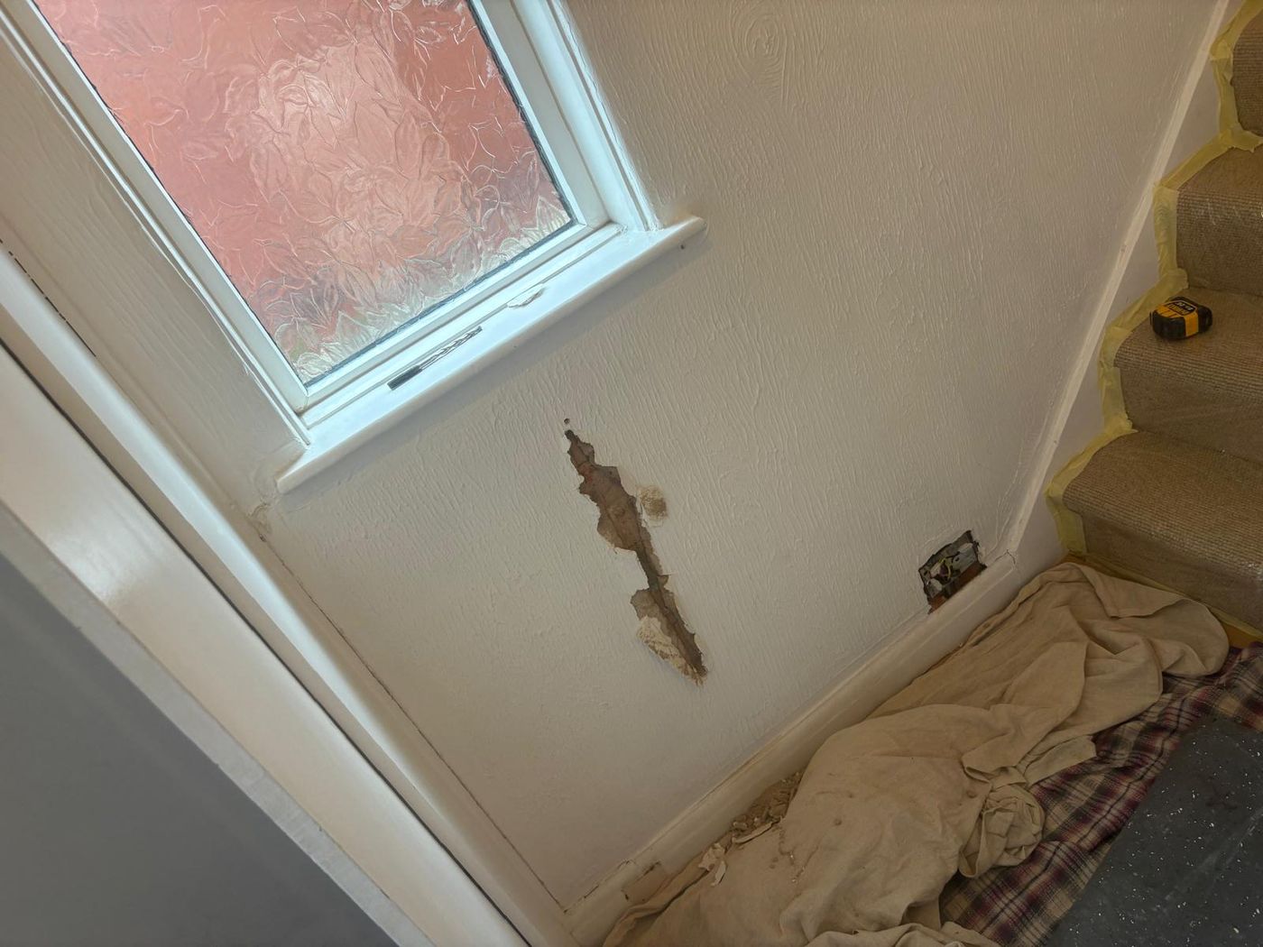 A section of blown, cracked plaster on a painted wall below a window