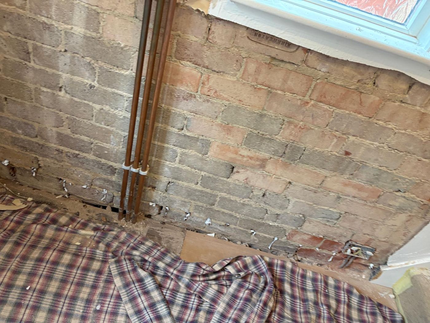 Exposed brickwork with damp proof course injection holes plugged along the mortar bed, copper pipework to one side