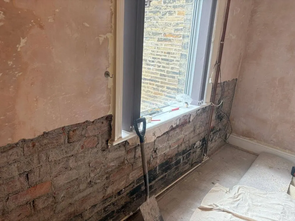Stained wall stripped back to exposed brick below a window during rising damp treatment